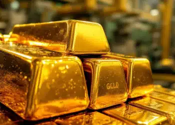 Barres d'or brillantes empilées avec un fond industriel flou.