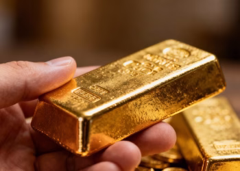 Main d'or tenant une barre d'or brillante.