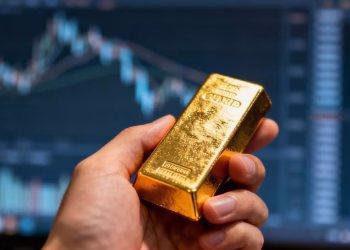 Main d'or tenant une barre d'or devant un écran d'ordinateur.