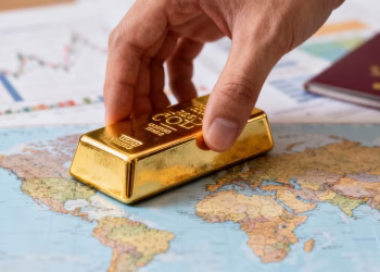 Main d'une personne plaçant une barre d'or sur une carte du monde.