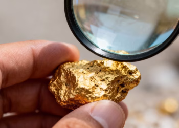 Main d'or examinant une pépite d'or avec une loupe.