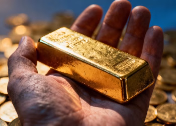 Main d'or tenant une barre d'or brillante avec des pièces.