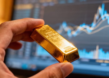 Main d'or tenant une barre d'or devant un écran numérique.