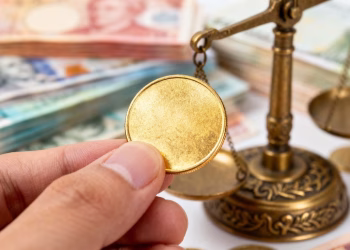 Main d'or tenant une pièce d'or, avec des billets flous.