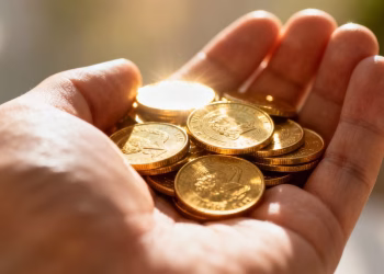 Main d'une personne tenant des pièces d'or brillantes.