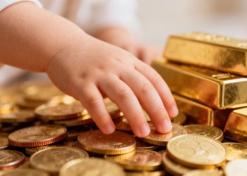 Main d'enfant touchant des pièces d'or et des lingots.