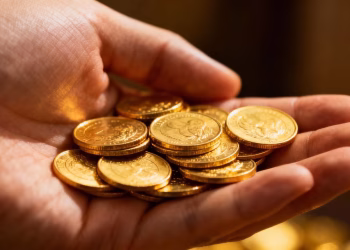 Main d'une personne tenant des pièces d'or brillantes.
