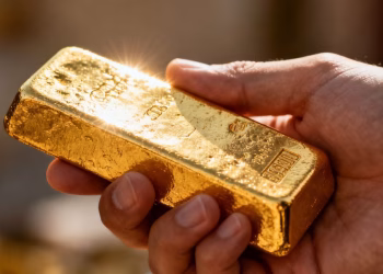 Main d'or tenant une barre d'or brillante.