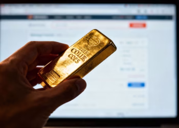 Main dorée tenant une barre d'or devant un écran d'ordinateur