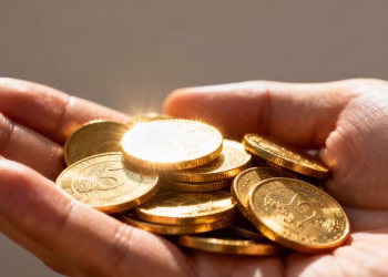 Main d'une personne tenant des pièces d'or brillantes.