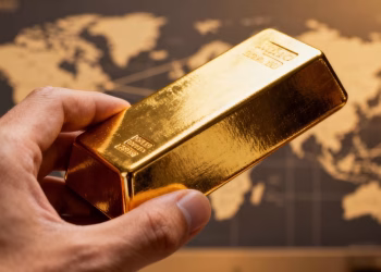 Main d'or tenant une barre d'or avec carte du monde floue.