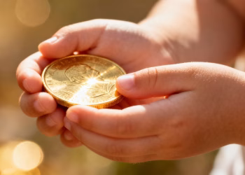 Mains d'enfant tenant une pièce d'or brillante.