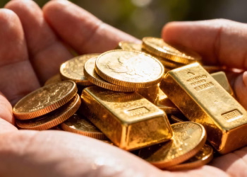 Main d'or tenant des pièces et des lingots d'or.