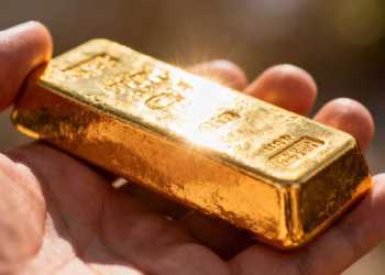 Main d'une personne tenant une barre d'or brillante.