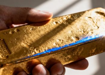 Main d'or tenant une barre d'or brillante.