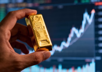 Main d'or tenant une barre d'or avec un graphique boursier flou.