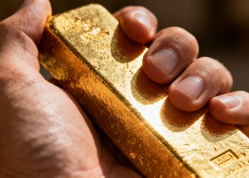 Main d'or tenant une barre d'or brillante.