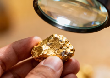 Main d'or examinant une pépite d'or avec une loupe.