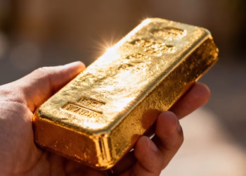 Main d'une personne tenant une barre d'or brillante.