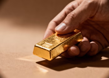 Main dorée tenant une barre d'or brillante.