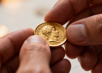 Main d'un numismate examinant une pièce d'or de collection.