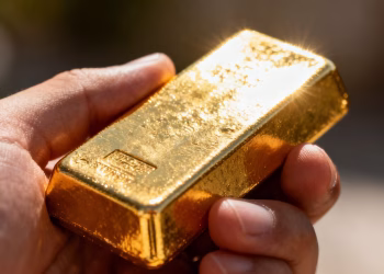 Main d'or tenant une barre d'or brillante.