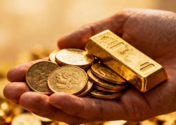 Main d'or tenant des pièces et des lingots d'or.