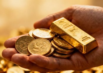 Main d'or tenant des pièces et des lingots d'or.