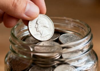 Main d'une personne plaçant une pièce d'argent dans une tirelire.