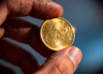 Main d'or tenant une pièce d'or, arrière-plan flou.