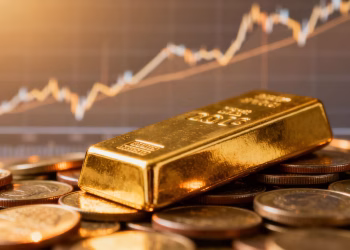 Lingot d'or sur des pièces, avec des graphiques de prix flous en arrière-plan.