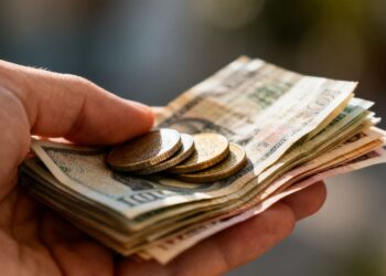 Main d'une personne tenant des pièces et des billets.