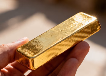 Main d'or tenant une barre d'or brillante.