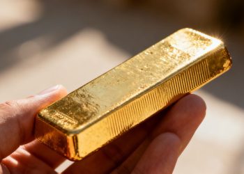 Main d'or tenant une barre d'or brillante.