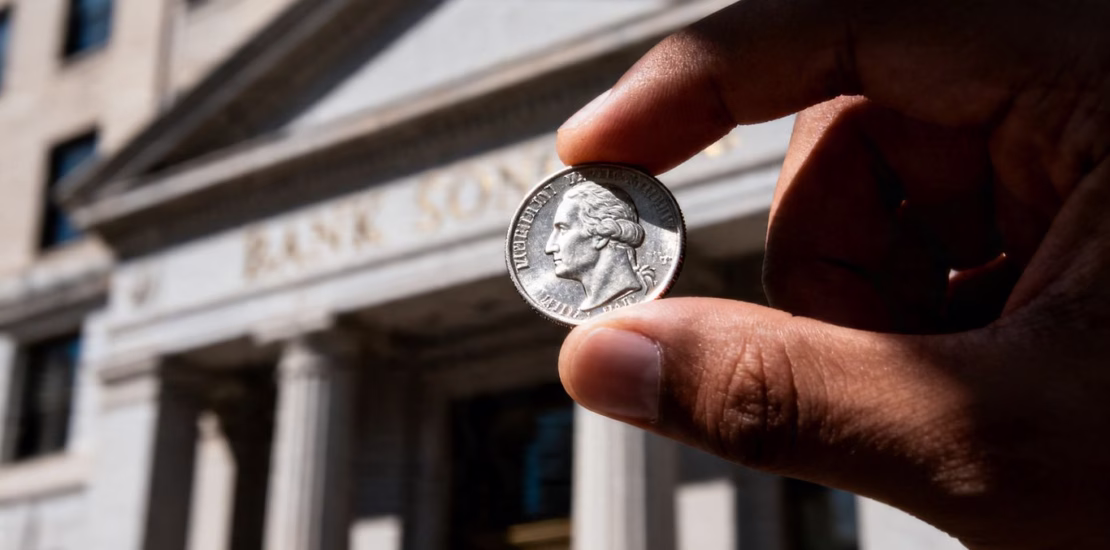 Main d'argent tenant une pièce d'argent devant une banque.