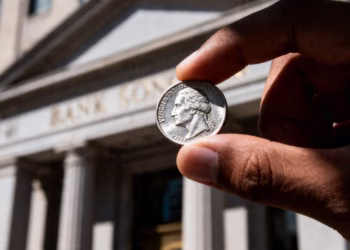 Main d'argent tenant une pièce d'argent devant une banque.