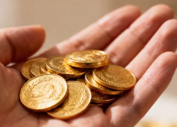 Main d'or tenant des pièces d'or brillantes.