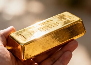 Main d'or tenant une barre d'or brillante.