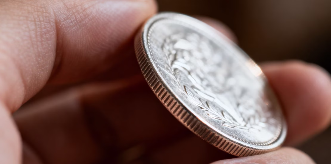 Main d'une personne tenant une pièce d'argent brillante.