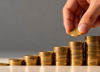 Main d'investisseur plaçant une pièce d'or sur une pile.