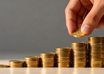 Main d'investisseur plaçant une pièce d'or sur une pile.