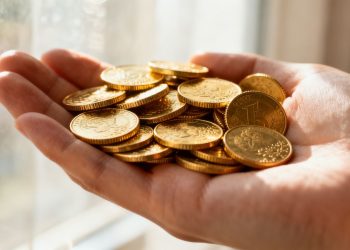 يد ذهبية تحمل عملات ذهبية لامعة.