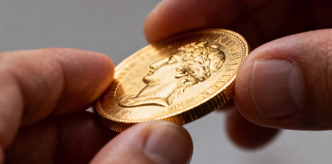 Main d'un numismate examinant une pièce d'or de collection.