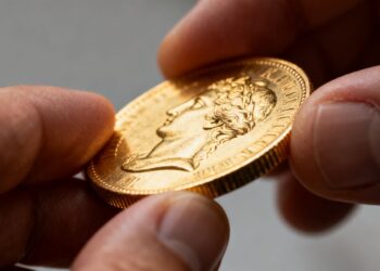 Main d'un numismate examinant une pièce d'or de collection.