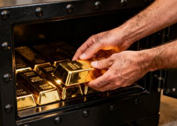 Mains plaçant des lingots d'or dans un coffre-fort.