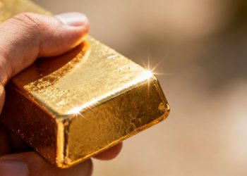 Main d'or tenant une barre d'or brillante.